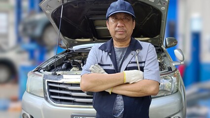 A professional auto mechanic in service is standing with his arms folded holding a wrench in a...
