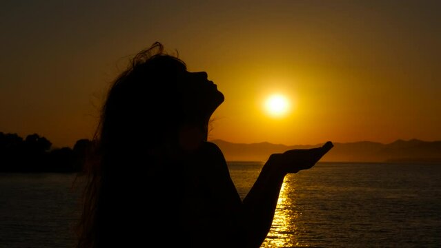 Child silhouette against amazing evening. A view of praying young girl stand on the beach against amazing bright sunset.