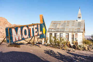 Antique motel sign pointing to abandoned church in the Nevada desert at sunset
