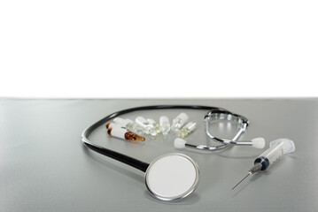 a stethoscope enveloping several ampoules and a syringe next to it on a gray table with a copy space background