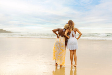 back portrait of multiracial couple of two girls leaning on each other contemplating the sea during...