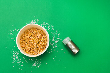 Wok noodles and salt shaker on a green background. Please add salt to your food in moderation. Too much salt in food is harmful to health. Flat lay