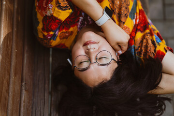 Relaxed and happy Asian woman enjoying listening to music on headphones while lying on a park bench. Casual young woman with closed eyes wearing headphones relaxing to music in a public park