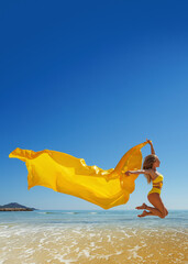 Happy young woman with a yellow light one Cloth jumping at sand beach. Relaxing, fun, and enjoy holiday at tropical paradise beach with blue sky. Girl in summer vacation. Poster.
