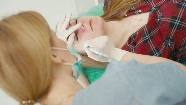 The doctor removes small blood vessels on the client's face with a laser. Cosmetology procedure with observance of sterility. High quality 4k footage