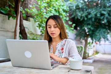 Fototapeta premium Young woman working on a laptop at a table outside on a patio at home