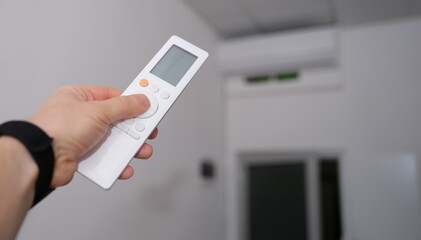 Hand with remote control is directed to air conditioner in room. Climate control indoor concept