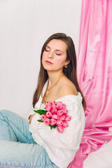 Beauty photoshoot of a brunette woman with her eyes closed holding pink flowers. Spring vibes, trendy, modern, editorial.