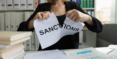 Businesswoman tears up sheet of paper with sanctions inscription. Economic sanctions against...