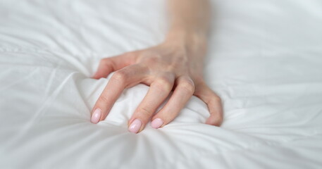 Fototapeta premium Woman hand tightly grips white sheet on bed. Nightmares and temper tantrums in the morning