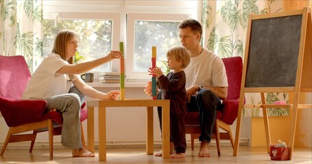 Parents and child enjoy quality time together in child's room, building with blocks. Warm...