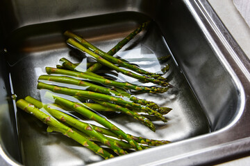 Asparagus soaking in water  in sink prior to additional preparation an cooking.
