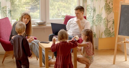 Work and family life. Father sits with laptop, children play around him. Despite being occupied, he remains present and engaged with family. Balancing professional responsibilities with family time