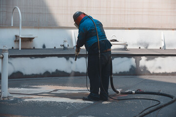 Male worker surface corrosion roof plate preparation by sand blasting of tank