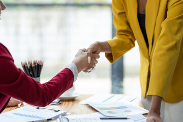 Close-up of two businesswomen shaking hands over a desk, symbolizing a successful agreement or partnership in a professional setting.