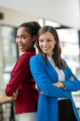 Two diverse businesswomen standing back-to-back, projecting confidence and partnership in a modern office space.