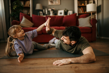 A little girl and her dad are on the floor in the living room lying down on stomachs after a hard home workout