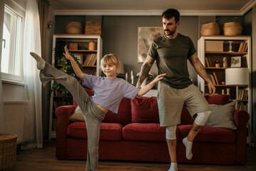 A little girl teaching her dad how to balance and dance in modern living room - obrazy, fototapety, plakaty