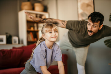 A little girl and her father during a home workout learning how to balance - obrazy, fototapety, plakaty