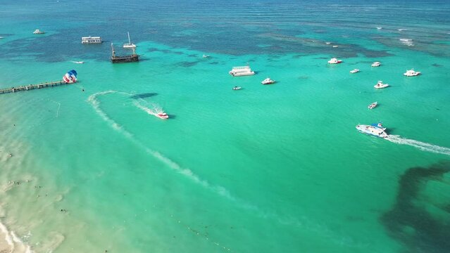 Aerial scenic view of Caribbean Sea featuring boats, parasailing, and water-based recreational activities for tourists, set against backdrop of turquoise waters. Dominican Republic, Punta Cana
