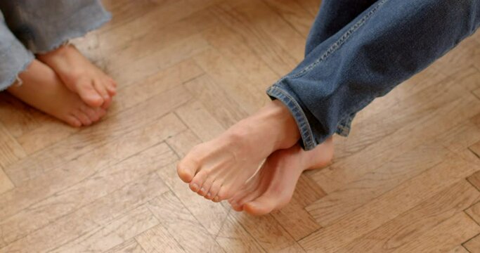 Bare male and female feet rest comfortably on the smooth parquet floor, exuding a sense of relaxation and intimacy. Warmth of the wood contrasts with the cool touch of the skin. Human body details.