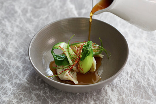 Dumplings and pak choi with the broth being poured