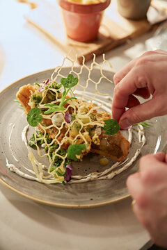Adding the finishing touches to a fine dining dish of fried fish, crushed peas and potato lattice