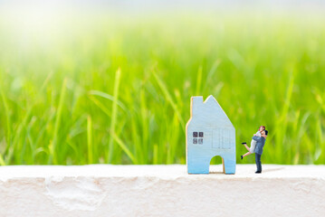 Miniature couple with blue wooden house model over blurred green grass background, real estate business