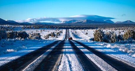 Frozen highway from Grand Canyon National Park to Williams Arizona on a cold sunny winter morning. Snow covered lanes in wide american landscape with oncoming truck. Symmetric panorama of wide scenery - obrazy, fototapety, plakaty