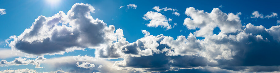 Cloud panorama on a sunny day with white and gray clouds, sun and blue sky. Wide angle shot in...