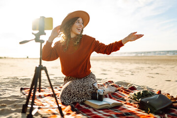 Female blogger recording video using smartphone on tripod on the seashore. Travel, technology...