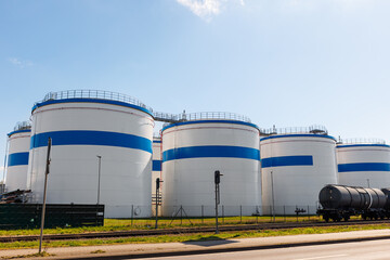 Row many large industrial fuel storage white tanks clear blue sky background on sunny day. Oil storage refinery depot liquid facilities. Energy hazmat railroad transportation storage and distribution