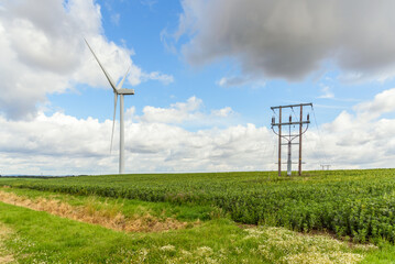Wind turbine and electricity lines in a cultivated field in the English countryside on a partly cloudy summer day