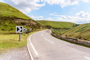 Chevron road signs on a sharp bend along a winding mountain pass road in England on a partly cloudy...