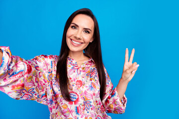 Photo of cheerful positive lady dressed print blouse tacking selfie showing v-sign isolated blue...