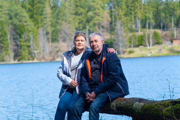 A couple of seniors are sitting on the log near the blue lake