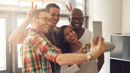 Diverse businesspeople making funny faces while taking a selfie together in a creative office....