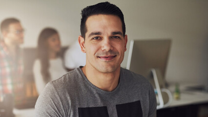 Positive young office worker looking at camera while his three diverse colleagues are in the background talking