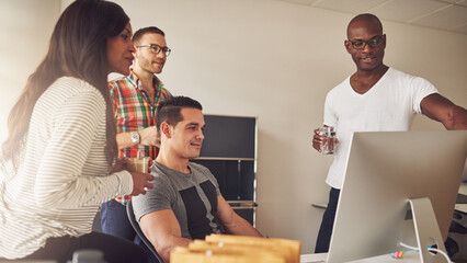 Focused diverse entrepreneurial team standing together around a computer screen they are all looking at. A man points at the screen to show the group something