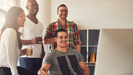 Man showing something on his computer to his three diverse colleagues. They laughing at each other and are happy about what they see on the screen