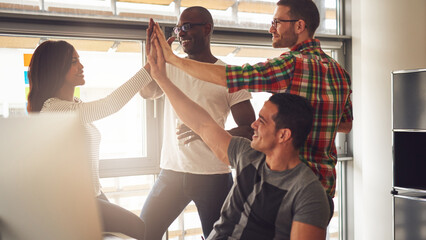 Four diverse coworkers stand together in an office community. They are happy and give each other a high five. They celebrate a win together while they smile at each other