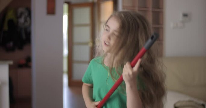 Enjoying Cleaning Playful Creative Child Dancing. Creative Teenage Girl Housewife Cleaning and Singing Using Broom Handle as Guitar Child Using Mop as Musical Instrument While Singing in Home.