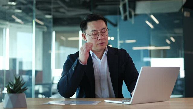 Worker feeling tired from typing on laptop and removing glasses to let eyes rest while sitting as desk. Male accountant touching forehead and having headache while working with financial reports.