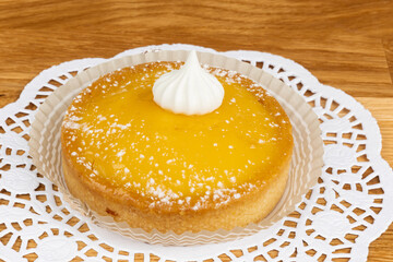 A yellow lemon tart with a bit of icing on a white doily - obrazy, fototapety, plakaty