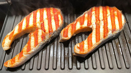 Salmon Fish Steak grilled on a grill pan with herbs. Black background. Top view