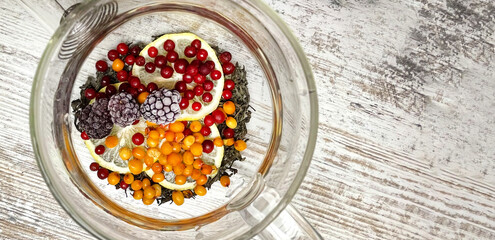 Multicolored fruit tea in a glass teapot with pieces of fresh fruit - lemon, red berries, sea...