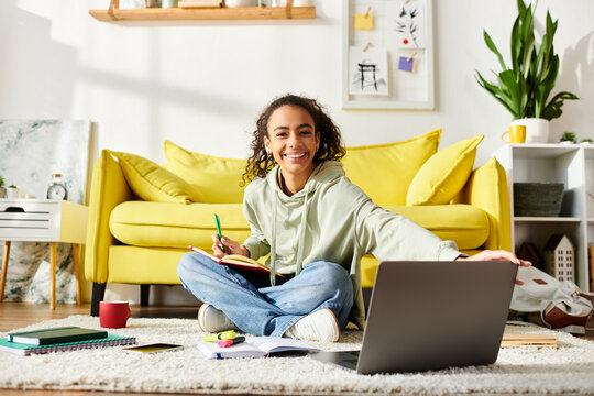 A teenage girl sits on the floor, focused on her laptop screen, actively engaged in e-learning at home.