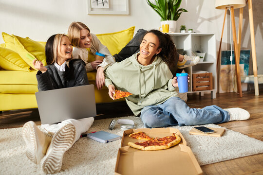 Diverse group of teenage girls sitting together on the floor, enjoying slices of pizza in a cozy home setting.