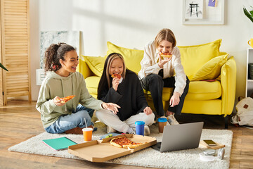 Three young women, representing diversity, sit on the floor enjoying slices of pizza together in a...