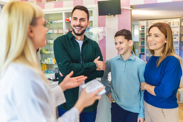 Cheerful pharmacist chemist woman giving vitamins to young family of three in modern pharmacy.